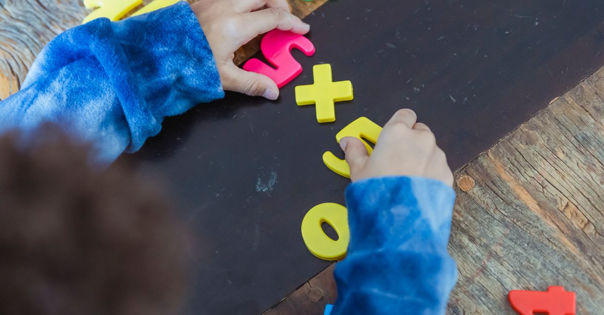 High angle of crop anonymous ethnic kid making mathematical multiplication with colorful plastic numbers during learning process